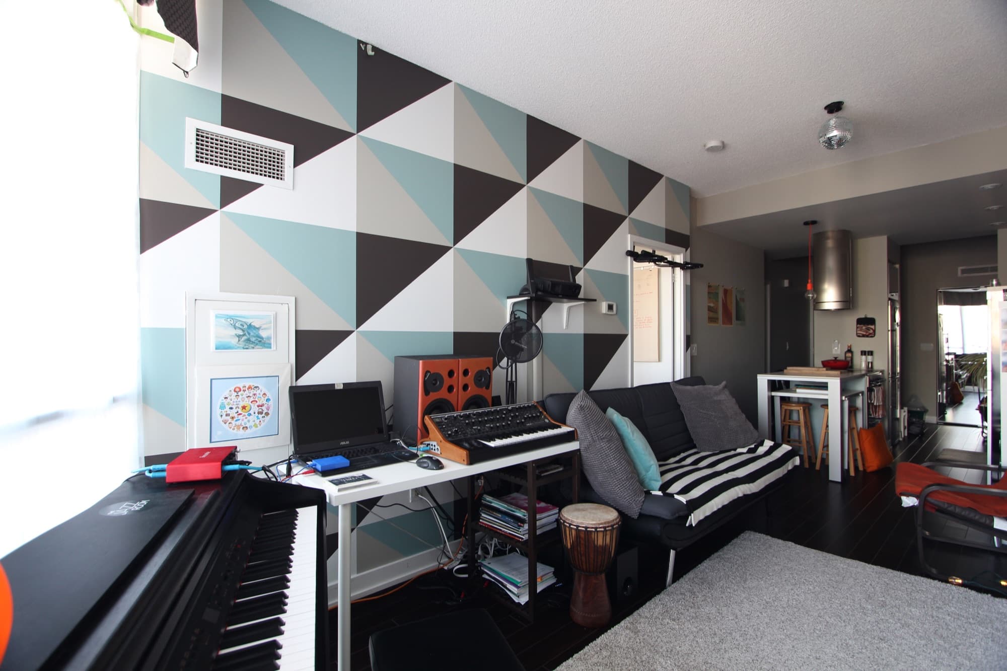 Triangulated wall mural in white, warm grey, charcoal, and dusty teal, set behind a piano and synthesizer in a Toronto condo.