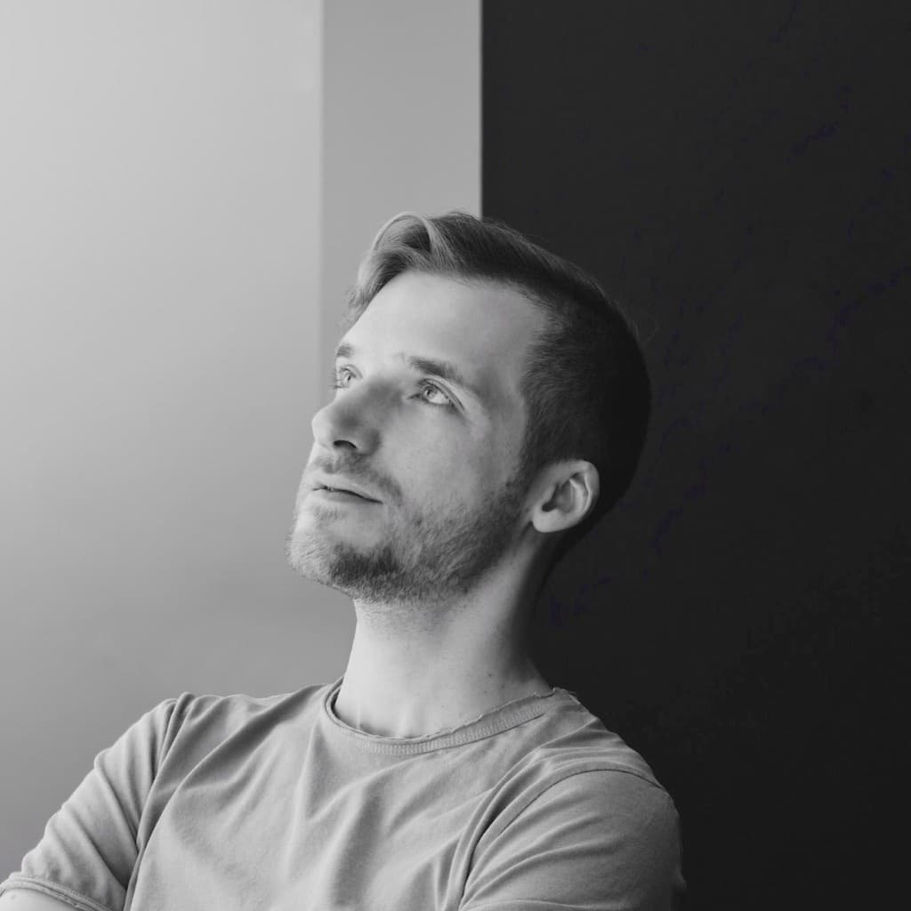Portrait of Chris, the artist behind Elevate Form, looking up against a wall divided diagonally between light and dark.